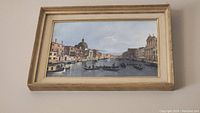 Framed print showing Italian or Greek style architecture beside a waterway with boats, in a golden frame.