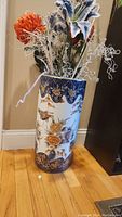 Large Japanese porcelain vase decorated with blue, white, gold floral and bird motifs, photographed standing on wooden floor.