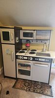 Front view of kids play kitchen with refrigerator, stove, sink, oven and microwave visible