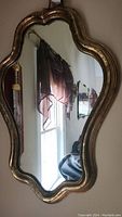 Ornate wall mirror with carved and gold-tone frame, clear reflective glass showing window and room details