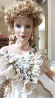 Close-up of the doll's face showing curly blonde hair, green eyes, pearl drop earrings, and pearl choker necklace with pink gem.