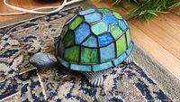 Turtle night lamp with stained glass shell in green and blue shades on a patterned rug.