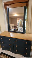 Wooden dresser with natural wood top and black painted body, featuring eight drawers with wooden knobs and mirror with black frame placed on top.