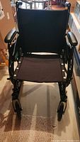 Front view of foldable wheelchair showing black fabric seat and backrest, armrests and front caster wheels.