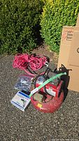 Photo showing pink heavy duty electrical extension cord coiled on the ground with small hardware items in packaging and part of the compressor visible.