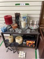 Overall view of candles, holders, glass and ceramic pieces placed on small dark table and floor beneath