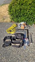 Photo showing the full layout of items: circular saw, framing tool pouch, extension cord, hammer, framing squares on concrete surface outside.