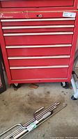 Front view of closed red six-drawer tool chest on wheels with pry bars on floor