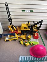 Overview photo showing all toys in the lot including the Tonka crane digger, Fisher-Price trucks, Lift & Load set, and pink hard hat.