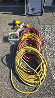 Overview of four coiled hoses (two yellow, two red), pneumatic spiker and palm nailers, plastic container of spikes