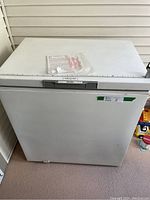 Front view of white Danby chest freezer with manual and cord on top, measuring tape indicating width.