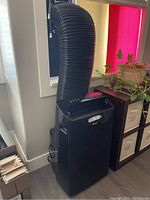 Front view of black Danby portable AC unit with flexible exhaust hose attached to window