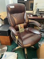 Front angled view of the brown leather office chair showing padded seat, backrest, armrests, and five caster wheels.