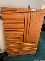 Front view of oak tall boy dresser showing drawer fronts and cabinet door closed