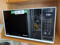 Front view of Panasonic NN-SC64MW microwave with a black glass door and white frame set on a wooden cabinet.