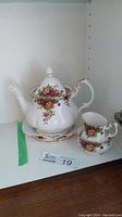 Teapot with lid on base, sugar bowl, and creamer pitcher arranged on shelf with Old Country Rose floral pattern and gold trim.