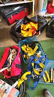 Wide shot showing two high-visibility vests in orange and yellow inside black and blue containers, a red duffle bag with beige webbing strips, and other parts of harnesses.