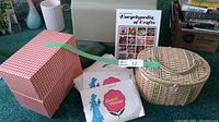 Overview of sewing patterns in sleeves, the encyclopedia book, and the red-checked storage box along with the wicker sewing supplies hamper.