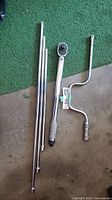 Layout of all tools including torque wrench, three ratchet extension bars, curved ratchet handle, and pin puller on floor with green carpet background.
