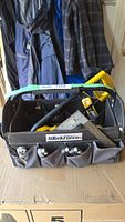 Front view of the full WorkForce tool tote filled with various tools including a yellow saw, carpenter square, and more, placed on a cardboard box.