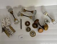 Full view of antique door hardware assortment on white background showing glass door handles, brass and wood knobs, painted hinges, and rosettes.