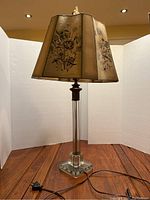 Full view of antique lamp showing floral paper shade and tall glass base with finial