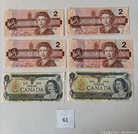 Lot showing all six Canadian banknotes laid out flat on white background, four $2 bills on top, two $1 bills below.