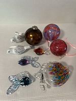 Lot arrangement showing four glass fish ornaments, three colored glass balls, and two white ceramic birds on a white surface.