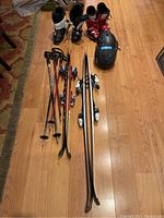 Full view of the skis, boots, poles, and helmets laid out on wood floor showing all items included in the lot.
