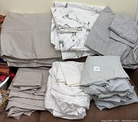 Photo showing multiple folded duvet covers and sheet sets in grey, patterned, and striped designs.