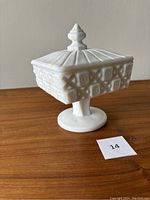 Side view of square milk glass candy dish on pedestal with lid and finial knob