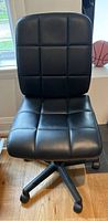 Front view of the black padded office chair, showing seat and backrest with square tufted pattern and caster base.