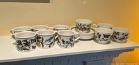 Full view of six coffee cups and four teacups with saucers arranged on a shelf, showing botanical floral patterns on white porcelain.