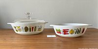 Two matching white Pyrex casseroles with colorful vegetable patterns; larger one includes glass lid