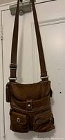 Front view of brown leather Roots crossbody bag showing multiple zippered and clasp pockets and adjustable strap.