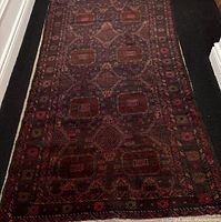 Full view of the rectangular wool rug showing its overall geometric patterns and dark color tones.