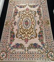 Full view of the handmade embroidered pink wool and cotton rug showing rectangular shape and floral scroll patterns.