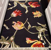 Full view of the rectangular rug showing floral pattern and fringe edges on a wooden floor.