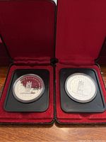 Two Canadian silver dollars, each in a black plastic holder inside red velvet-lined display cases. Both coins have the same design depicting the Senate Throne with inscriptions 'CANADA', 'DOLLAR', and 'THRONE OF THE SENATE' in English and French.