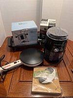 Overview of all items together showing Black and Decker griddle, Multi Chef crepe maker, Hamilton Beach Sno-Cone maker, herb chopping set, and fondue sets.