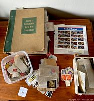 Photo showing the Denhof stamp album with wear, a container of loose stamps, and the 1997 US Football Coaches new sheet.