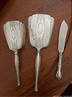Sterling silver hair brush, hand mirror, and Birks cake cutter laid on wood surface