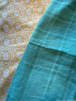 Close-up of yellow and white woven cotton tablecloth and turquoise linen tablecloth showing fabric texture and color contrast.