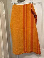 Orange linen tablecloth with vertical red stripes hanging on a hanger, showing color and fabric texture.