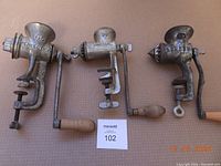 Photo of three antique meat grinders side-by-side showing Perfection, Universal, and London SPONG brands with visible rust.