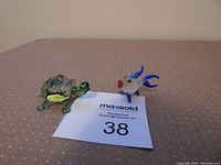 Photo showing the hand blown glass turtle figurine with painted details alongside the fish figurine on a beige surface.