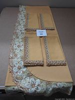 Full view of the gold tablecloth with large floral lace edging and 4 matching napkins with lace trim placed on top.