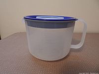 Side view of clear plastic measuring cup with blue lid and handle, placed on a pinkish polka dot table surface