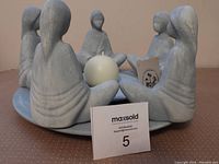 Pottery candle holder showing the six seated figures in a circle holding a white round candle.