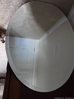 Oval mirror photographed flat on carpet showing its clear reflective surface and beveled edge.